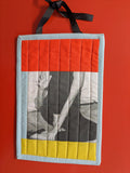 Quilted square with a printed design of a person sitting on a bench, hanging against a red background.