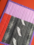 Quilt with a geometric pattern featuring hands and a red and purple border.