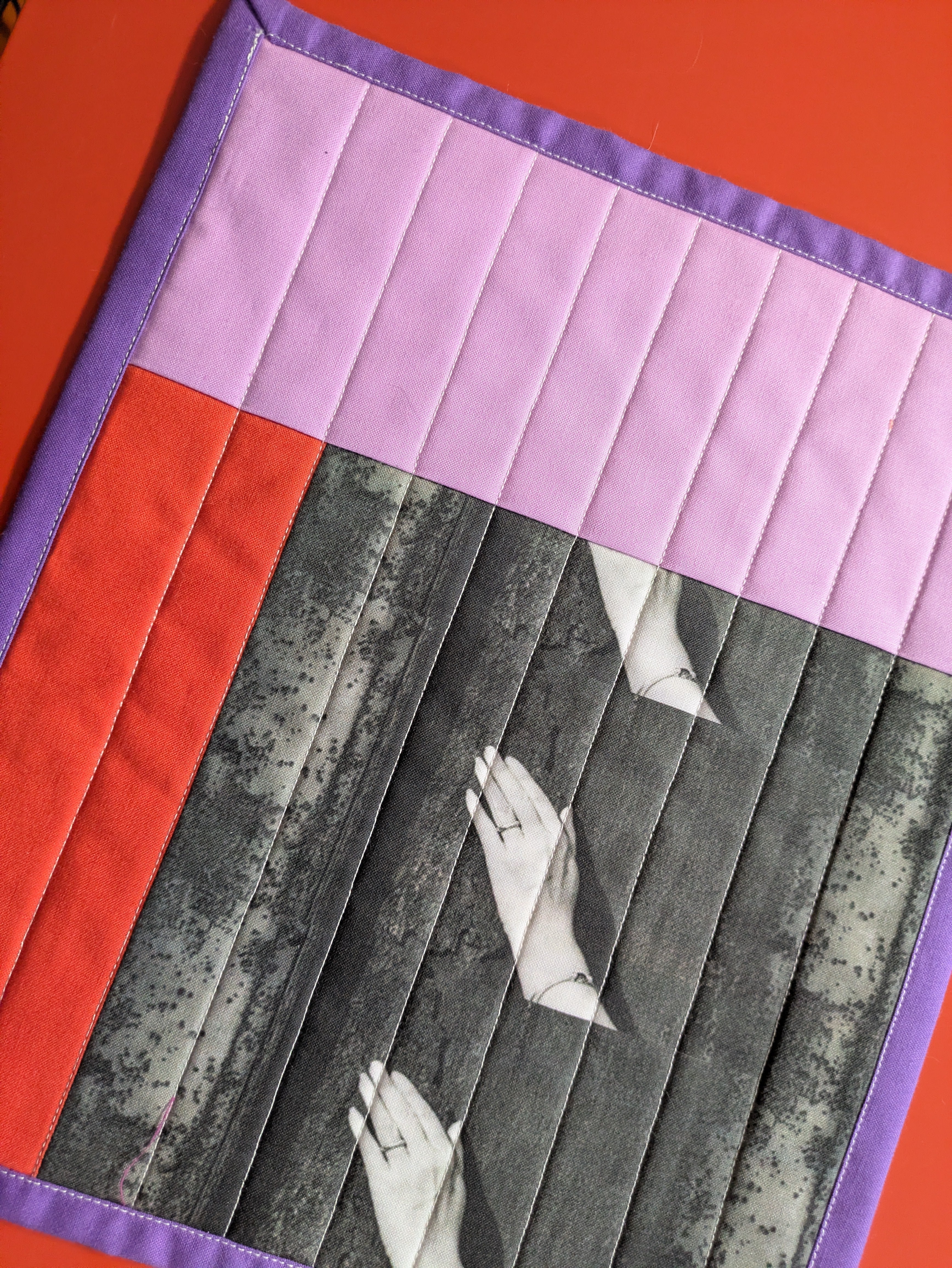 Quilt with a geometric pattern featuring hands and a red and purple border.