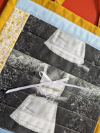Quilt with black and white photo of a person wearing a hat, tied with a white ribbon, on a textured surface.